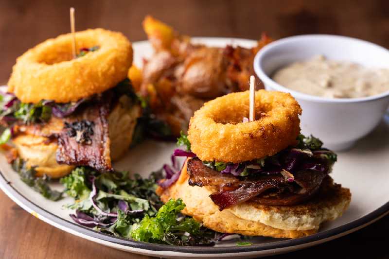 Savory Brisket Biscuit Sliders - Biscuit sliders topped with tender brisket, crispy onion rings, and fresh greens at Brekki Brekki, perfect for brunch or lunch seekers in Albuquerque restaurants.