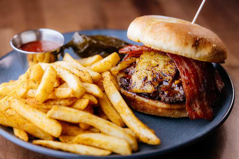 Gourmet Red Chile Hawaiian Burger with Fries - A gourmet burger topped with crispy bacon, grilled pineapple, and a flavorful red chile sauce, served with seasoned fries at Brekki Brekki. A must-try for anyone searching for lunch in Albuquerque or new restaurants near me.